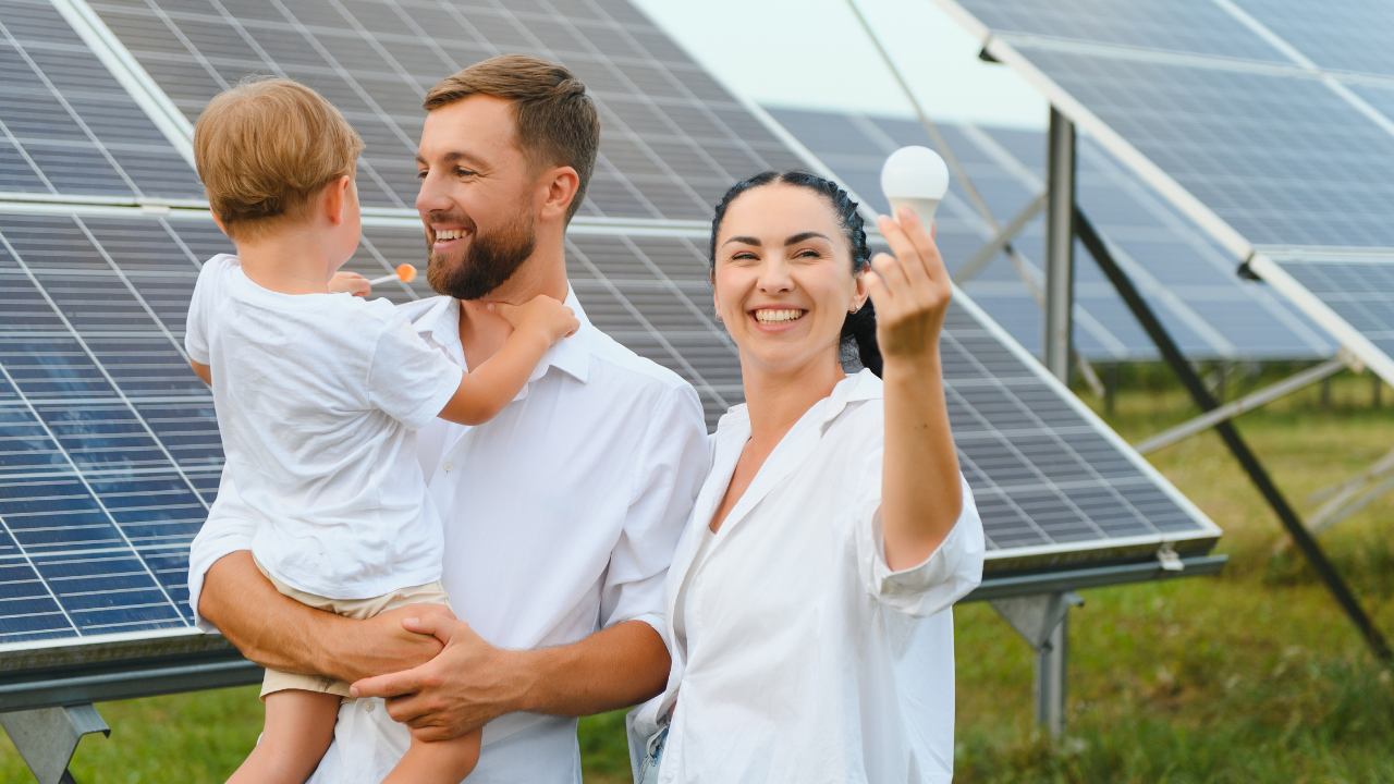 A cheerful family stands in front of solar panels, with the mother holding up a light bulb. The image highlights the benefits of clean energy through solar panel installation, emphasizing a bright and sustainable future for families.