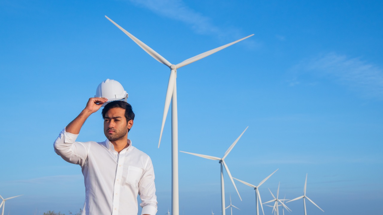 An American technician adjusts his helmet while standing before a field of turbines, reflecting the nation's commitment to clean energy solutions.