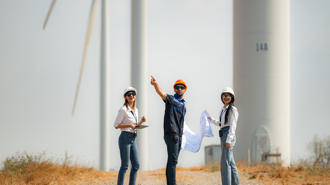 Tres profesionales revisan planos frente a aerogeneradores en funcionamiento, representando la planificación activa en energías renovables en España.