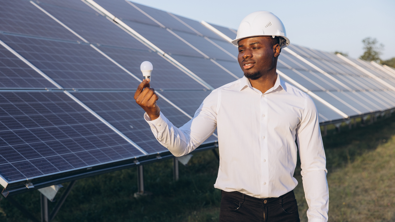 Un trabajador sostiene una bombilla mientras observa con atención los paneles solares. La imagen transmite reflexión sobre cómo aprovechar la energía sobrante paneles solares en soluciones prácticas y sostenibles.