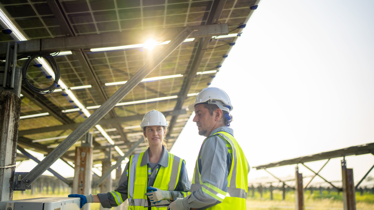 Dos técnicos en chalecos reflectantes trabajan bajo una estructura de paneles solares. Su interacción técnica sugiere un enfoque profesional y local para gestionar la energía sobrante paneles solares con precisión operativa.