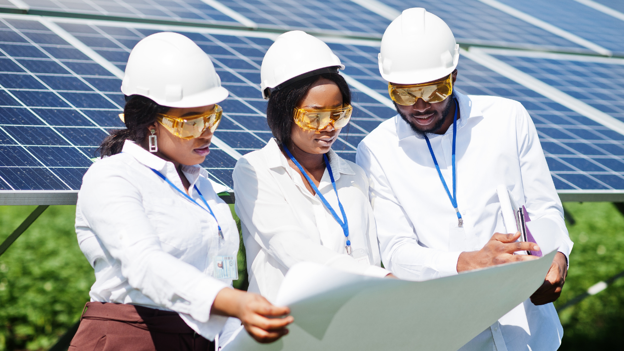 Tres personas observan detenidamente un plano frente a paneles solares. Su vestimenta técnica y actitud analítica reflejan una inspección minuciosa del sistema de tejas solares en un contexto de trabajo colaborativo.