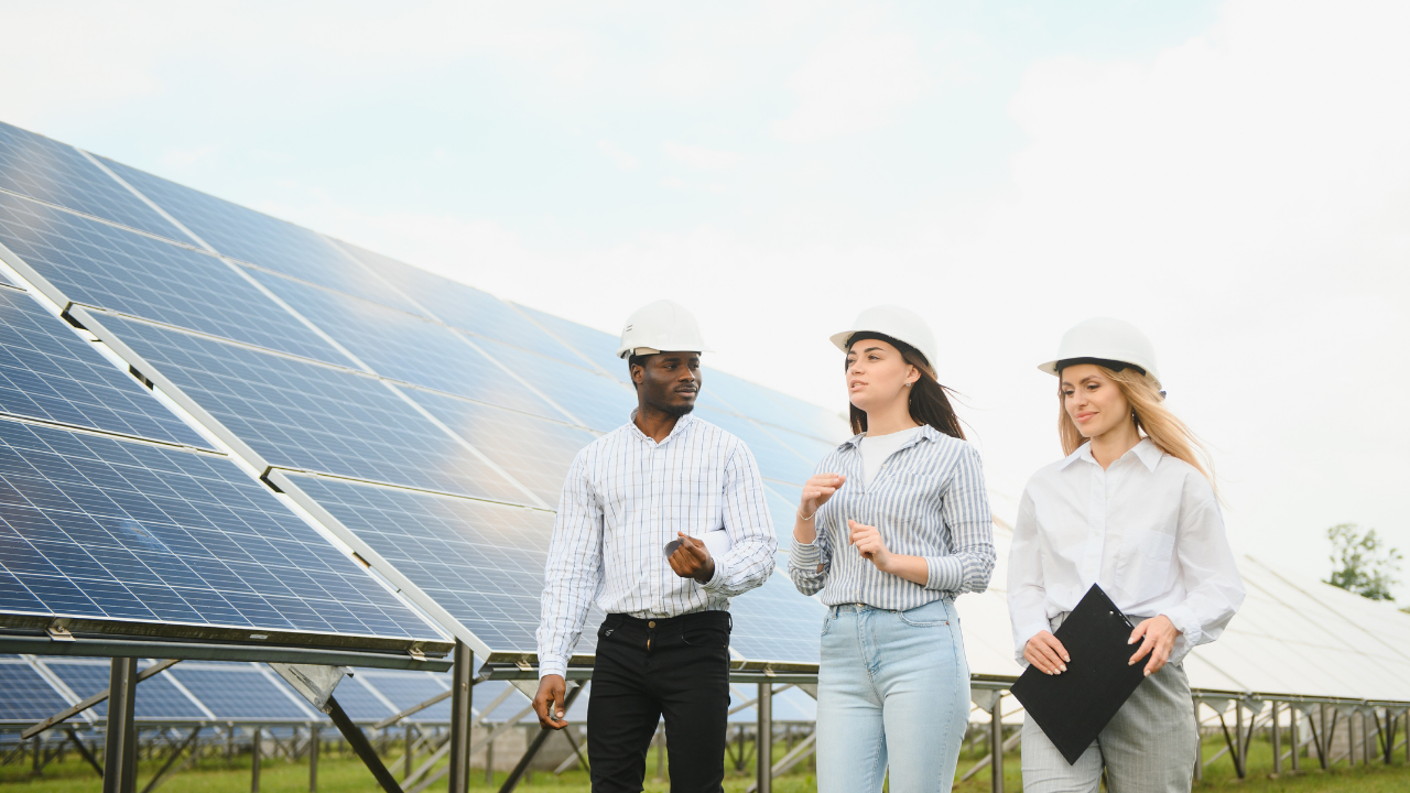 A group of professionals in white helmets walks alongside solar panels, engaged in conversation. The phrase "clean solar panels" emphasizes the ongoing commitment to sustainability in a collaborative and diverse work environment.