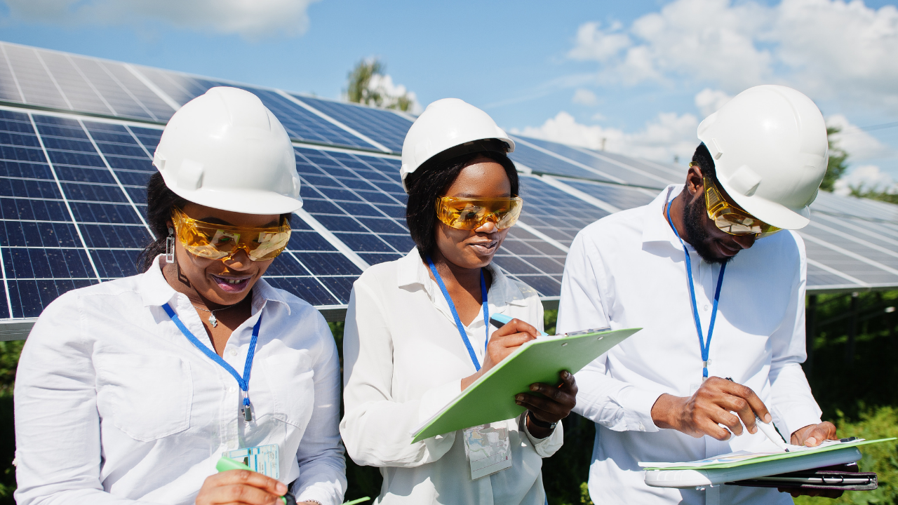 Tres técnicos con gafas de protección y carpetas anotan información mientras observan los paneles solares. "Limpiar paneles solares" refleja la meticulosidad en la revisión y mantenimiento de sistemas solares bajo cielos despejados.