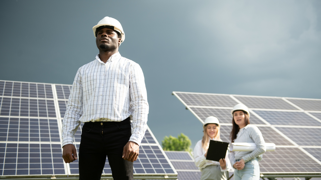 A confident engineer stands in front of solar panels under a dramatic sky, while two female colleagues collaborate in the background. The visual embodies leadership in clean technology, reinforcing the role of concentrated solar power.