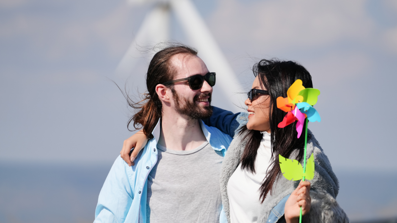 Una pareja sonriente sostiene un molinillo de viento colorido, conectando el juego con la comprensión visual de cómo funciona la energía eólica.