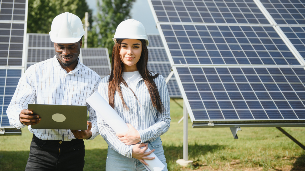 Un hombre y una mujer revisan planos y datos digitales frente a una gran hilera de paneles solares. "Paneles solares" expresa la sinergia entre innovación tecnológica y planificación estratégica en un entorno natural.