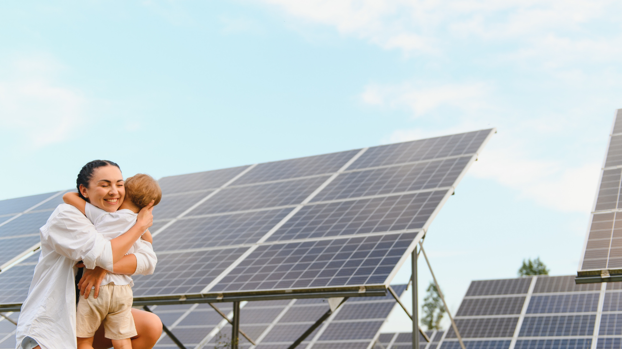 Una madre abraza a su hijo frente a paneles solares bifaciales, en un entorno natural y soleado. "Paneles solares bifaciales" sugiere un futuro sustentable que protege tanto el planeta como a las próximas generaciones.
