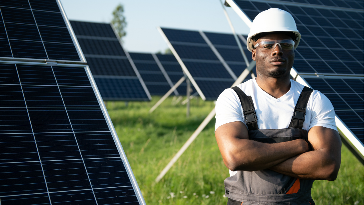 A solar field worker stands with folded arms among photovoltaic panels, wearing safety gear and exuding confidence. The scene highlights the human element behind concentrated solar power and its importance in sustainable infrastructure.