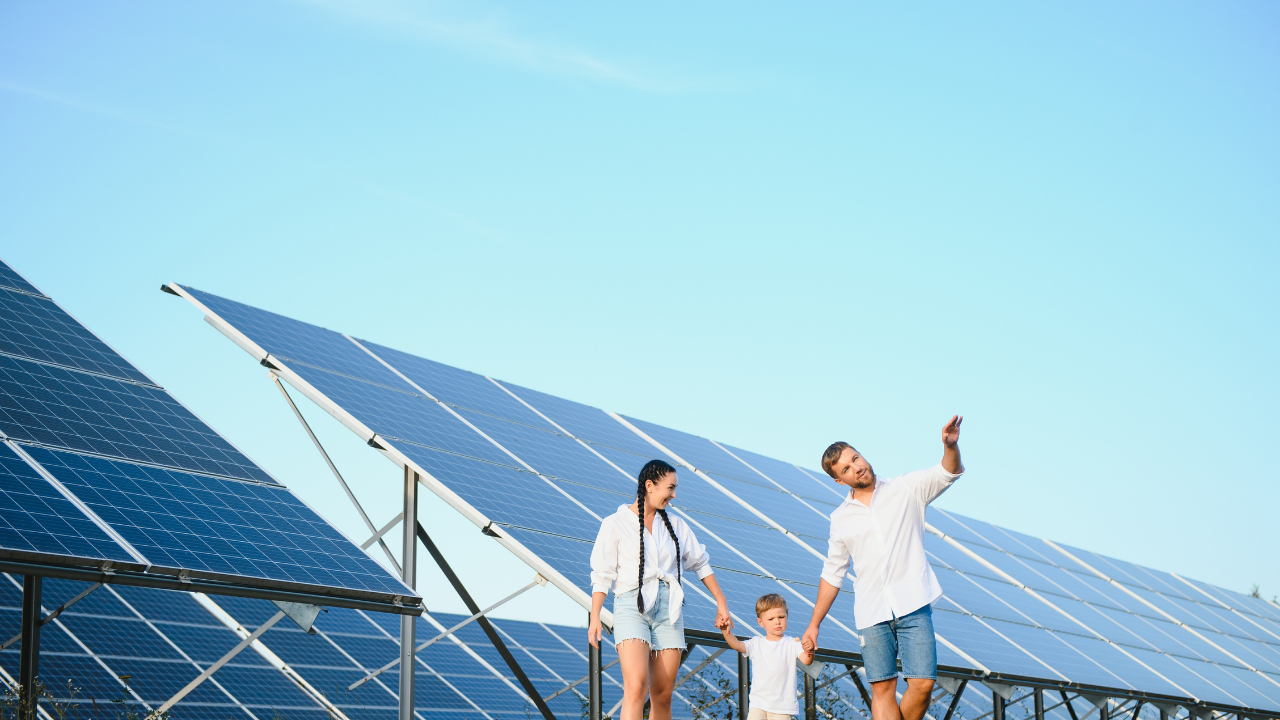 A family walks by an array of solar panels under a clear sky, the father pointing towards the installation. The phrase "orientation and tilt" reflects how panel positioning is essential for capturing maximum solar energy in daily life contexts.