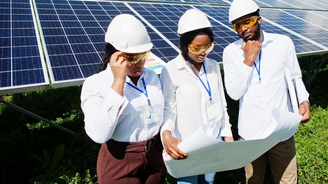 Tres técnicos estudian un plano con atención, protegidos por cascos y gafas de seguridad, frente a paneles solares. "Orientación e inclinación" enfatiza el análisis técnico requerido para una instalación precisa.