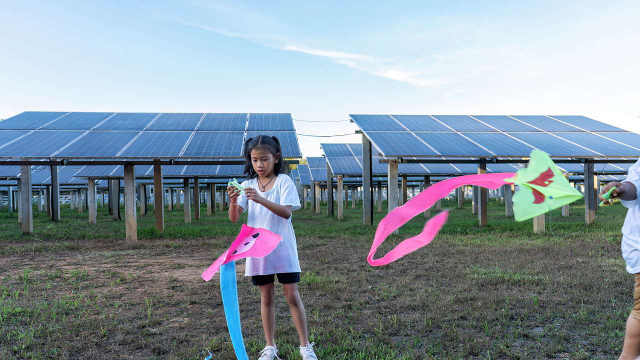 A young girl prepares a kite near an off-grid solar installation, with the panels elevated behind her. The phrase "off-grid solar installation" highlights the coexistence of sustainable energy and recreational outdoor spaces.