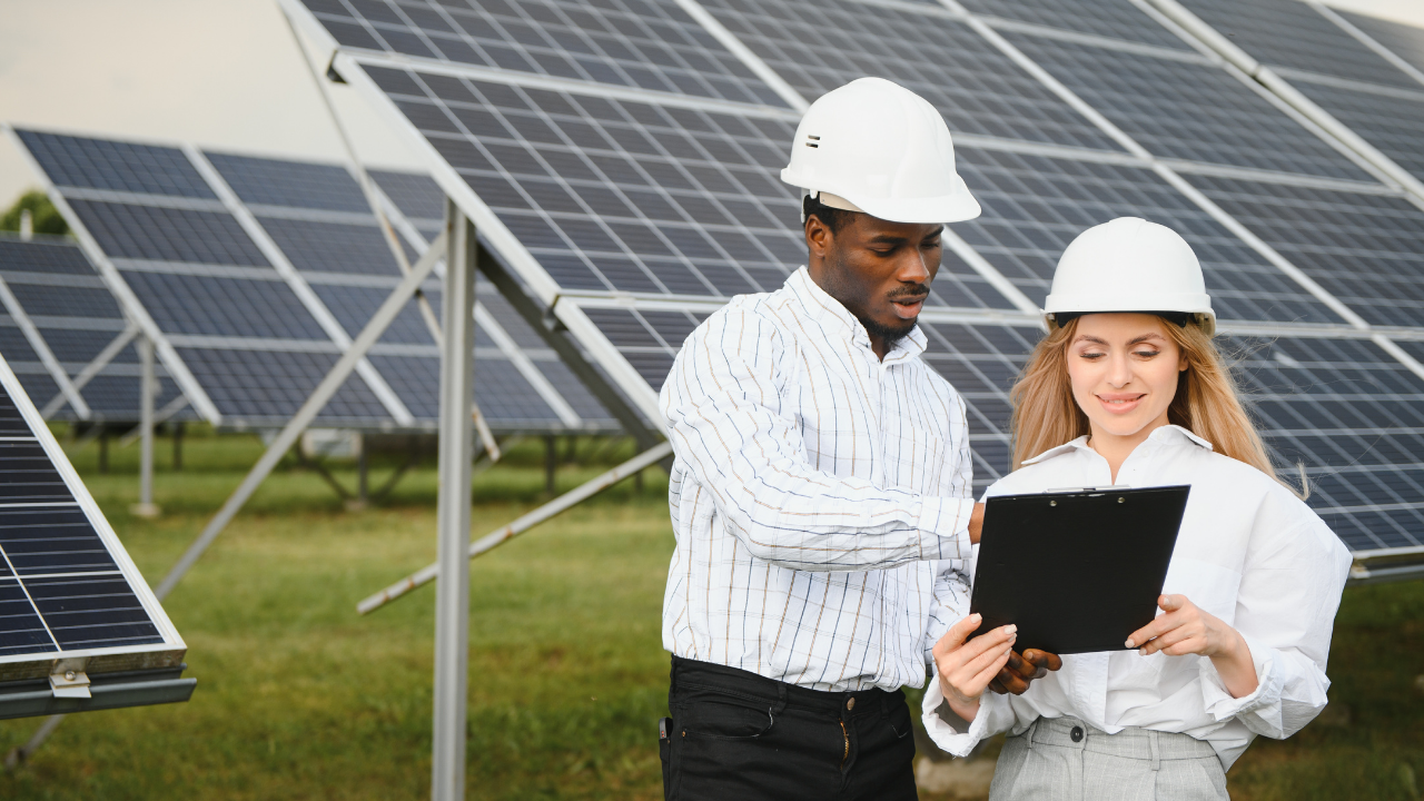 Two engineers in white helmets review data together at an off-grid solar setup. "Off-grid solar installation" emphasizes the autonomy and monitoring needed for decentralized energy systems.