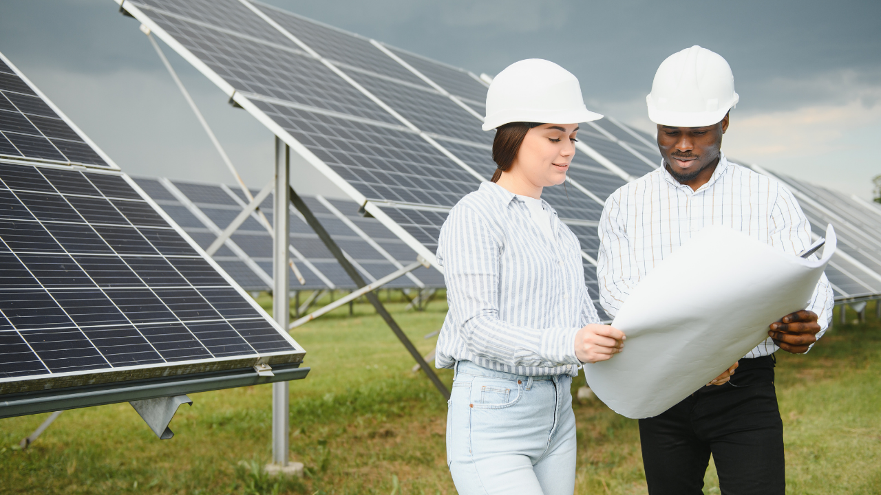 Dos ingenieros observan un plano técnico frente a paneles solares, con cielo nublado al fondo. "Instalación solar aislada" transmite planificación y adaptación a distintos entornos climáticos.
