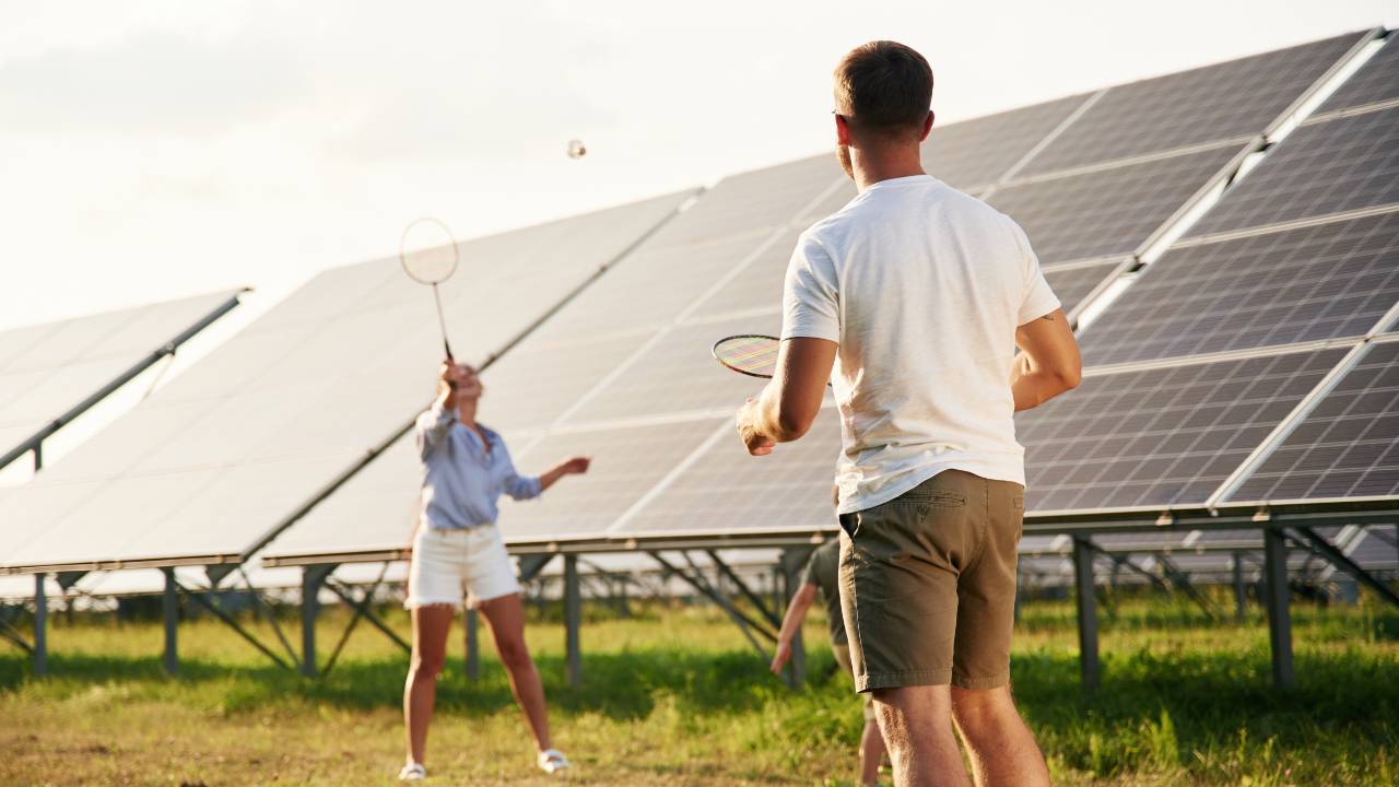 A couple enjoys a game of badminton near a solar installation, highlighting a lifestyle integrated with sustainable energy and the efficiency of solar panels.