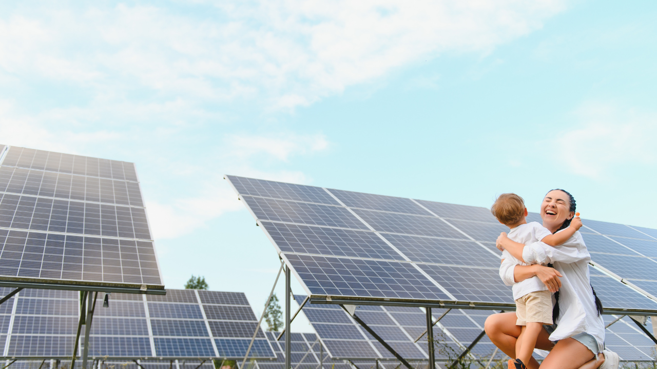 Una madre sostiene a su hijo en brazos con una gran sonrisa, rodeados de paneles solares, transmitiendo un mensaje de futuro limpio gracias a la eficiencia de tus paneles solares.