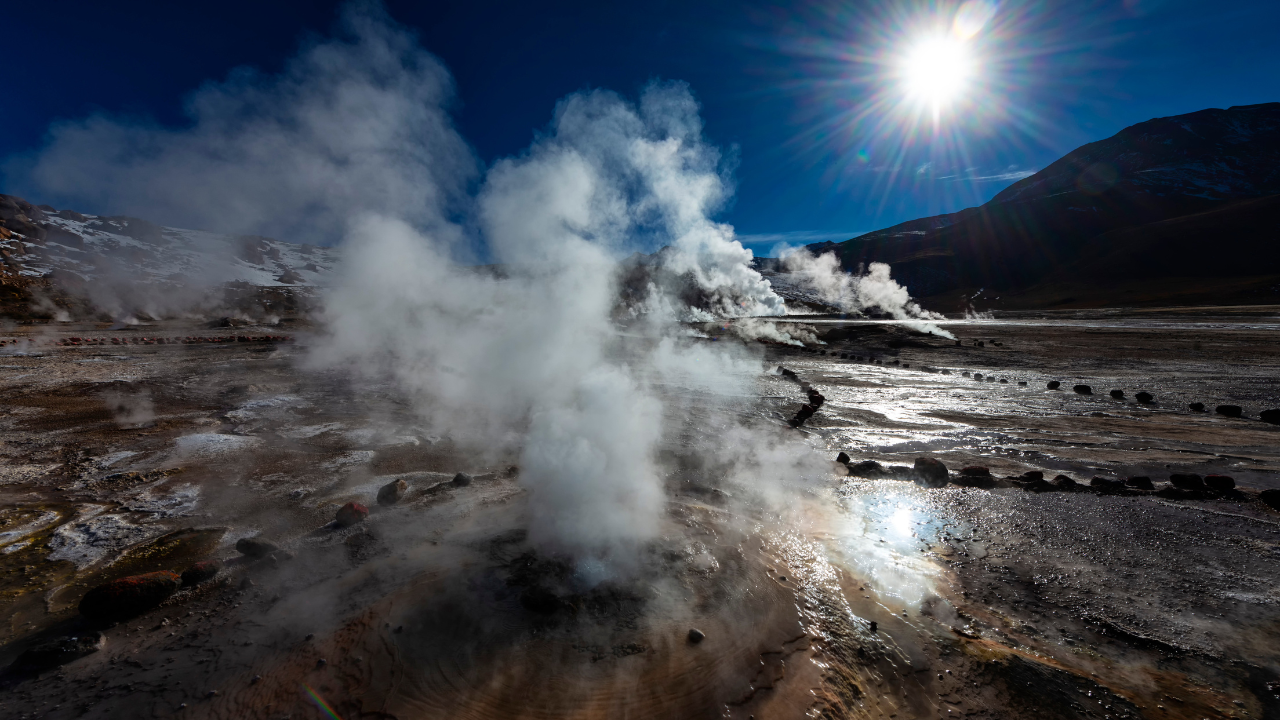 A dramatic geothermal field emits thick plumes of steam under the bright sun, capturing the raw force of geothermal energy in a highland landscape.