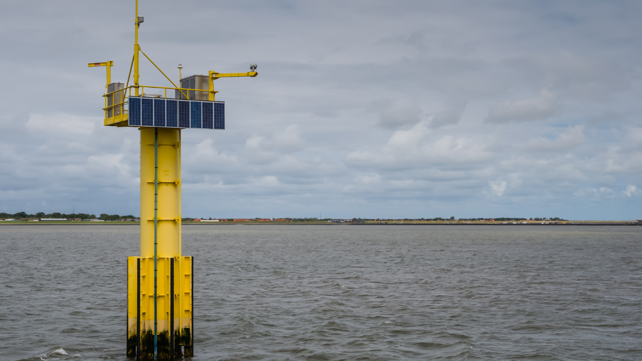 Una torre amarilla con paneles solares cerca del mar simboliza el monitoreo costero y su posible vínculo con la energía mareomotriz.