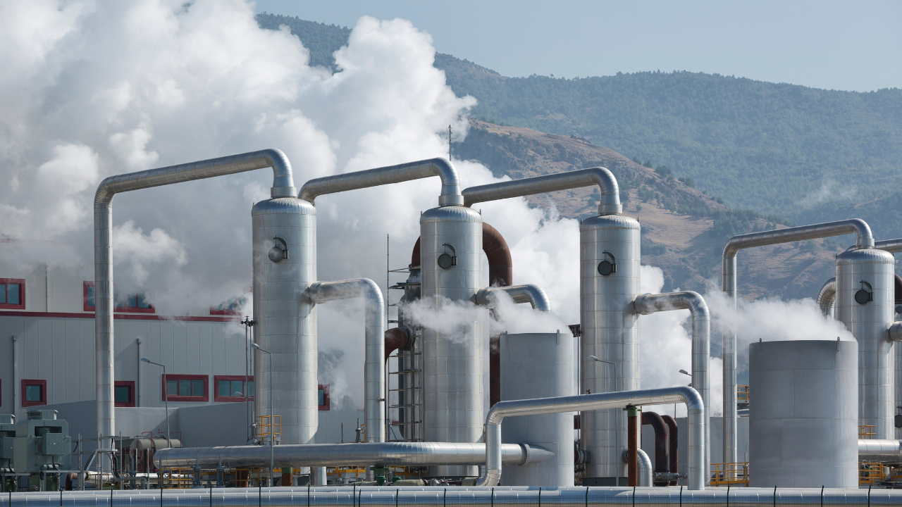Una planta industrial moderna con vapor blanco intenso representa el uso eficiente de la Geotermia en el hogar como fuente energética sostenible en entornos urbanos.
