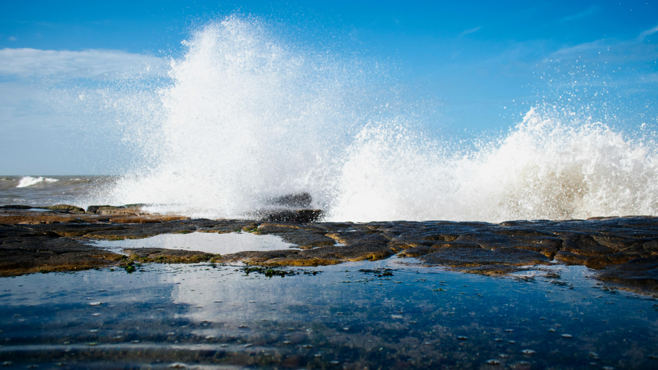 Ocean spray crashes dramatically against rocks, symbolizing the untapped force of wave energy available on the American shoreline.