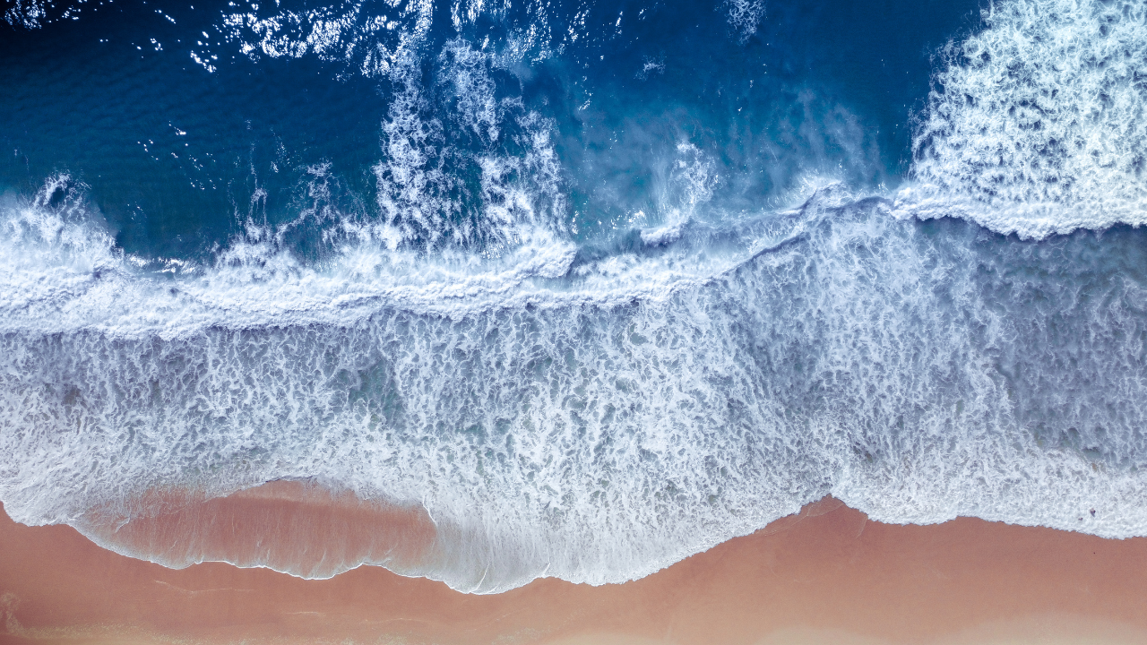 Una vista aérea muestra el oleaje constante sobre la playa, reflejando el flujo natural ideal para aprovechar la energía undimotriz.