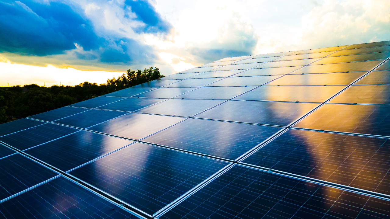 Paneles solares captan los últimos rayos del sol con reflejos en el cielo, ilustrando el avance de Uruguay en el uso de Aerotermia para energías renovables.