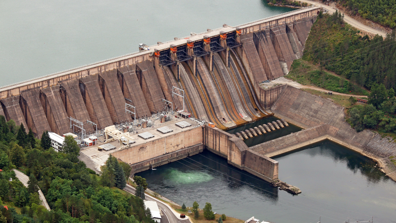 Vista aérea de una represa con vertederos amplios y zona de control técnico, representando la importancia de las centrales hidroeléctricas en el suministro energético.